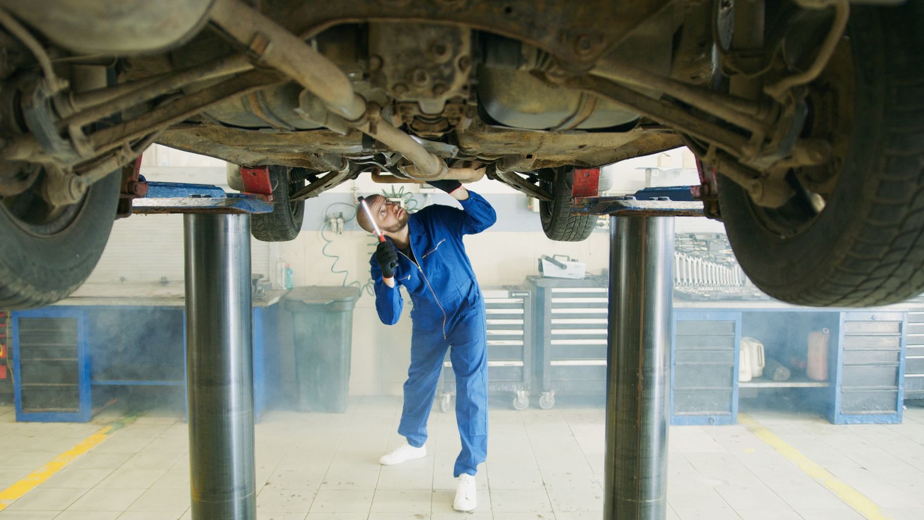 Mechanik w niebieskim kombinezonie ogląda podwozie auta w warsztacie