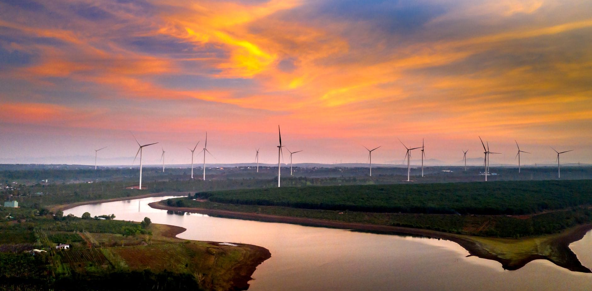 Turbiny wiatrowe nad rzeką i polami o zachodzie słońca