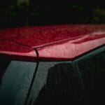 Powłoka hydrofobowa na szyby samochodowe: jak działa i czy warto ją nakładać? Czerwony dach samochodu pokryty kroplami deszczu uzyskanymi na hydrofobowej powł